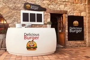 Fachada de um ambiente para restaurante a la carte com paredes texturizadas de tijolos, um balcão na frente e cartazes com escritas de Delicious Burguer e o símbolo de um hambúrguer