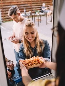 Mulher loira comendo batata frita de um food truck